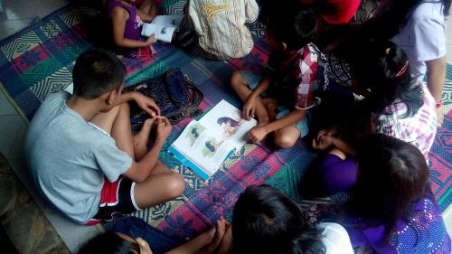 Anak-anak sedang menyimak buku secara berkelompok.